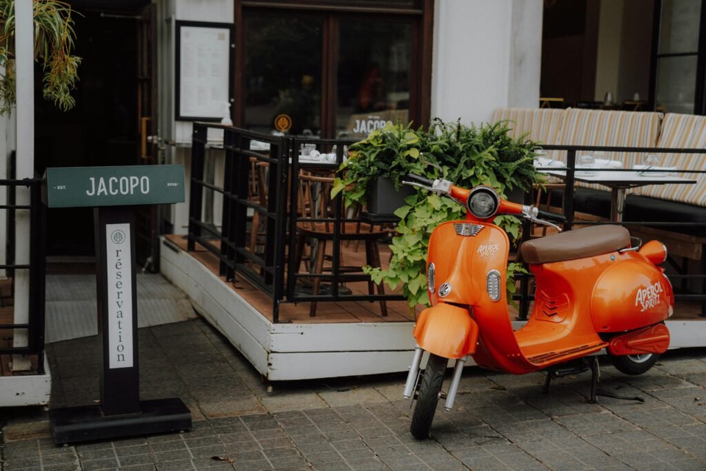 A bright orange scooter parked in front of Jacopo Café in Québec City. Charming outdoor seating.